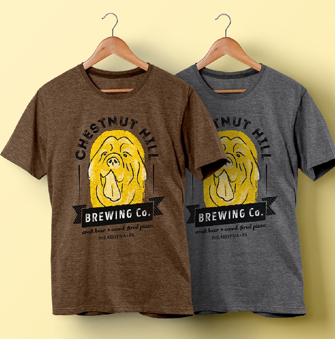 Two t-shirts hang side by side, one brown and one gray, both featuring a yellow dog illustration and the text "Chestnut Hill Brewing Co."