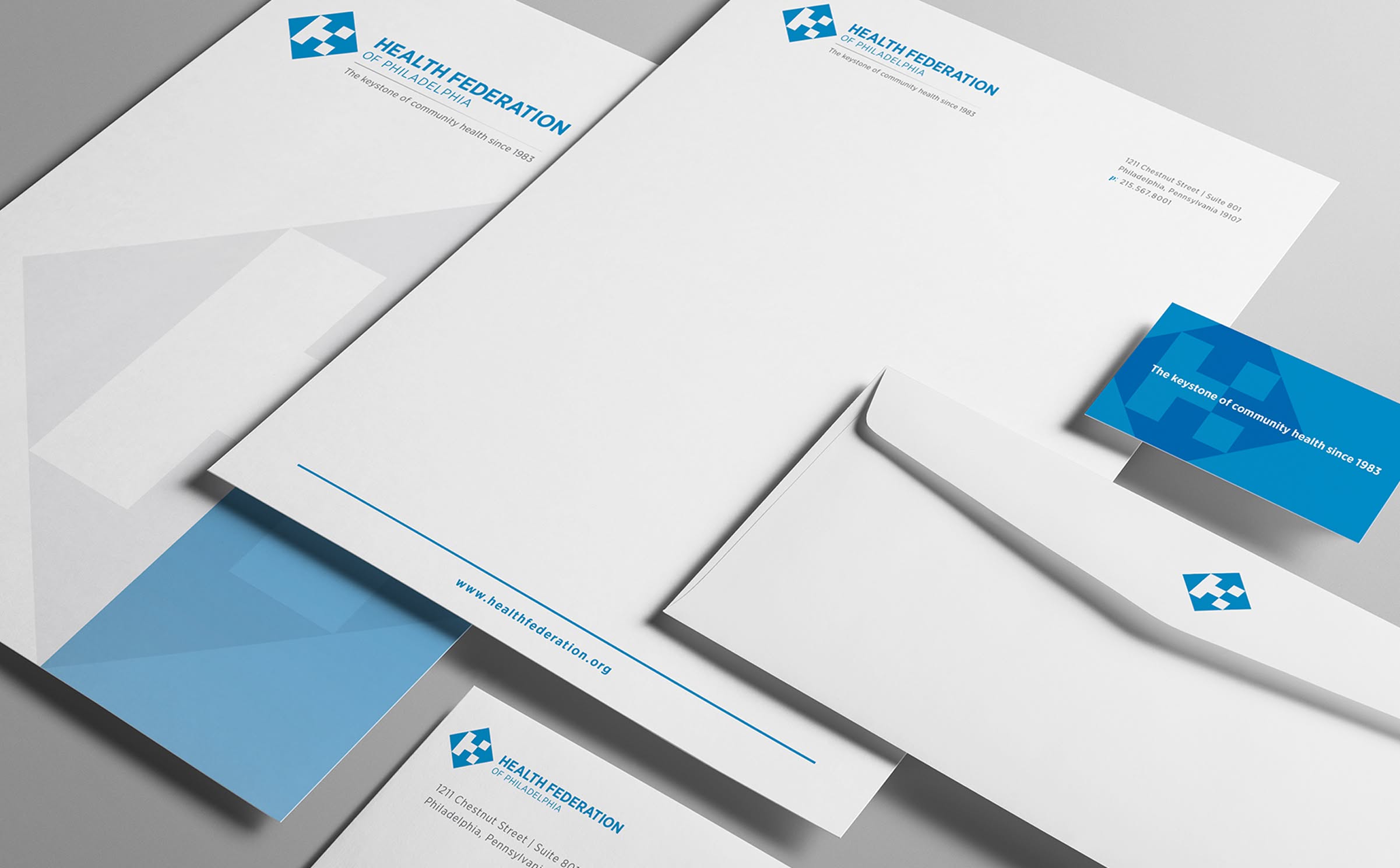 HealthFed-Stationery A set of Health Federation stationery featuring a white and light blue color scheme, including letterhead, envelopes, and business cards with a blue geometric logo.