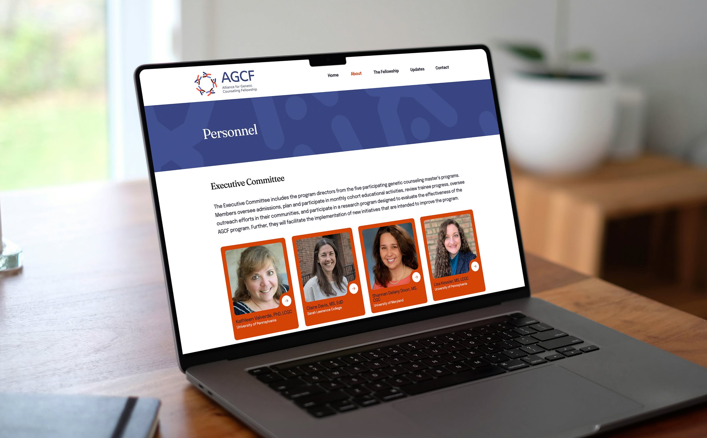 Laptop on a wooden table displaying the AGCF website, showcasing portraits of four women within red boxes in a "Personnel" section.