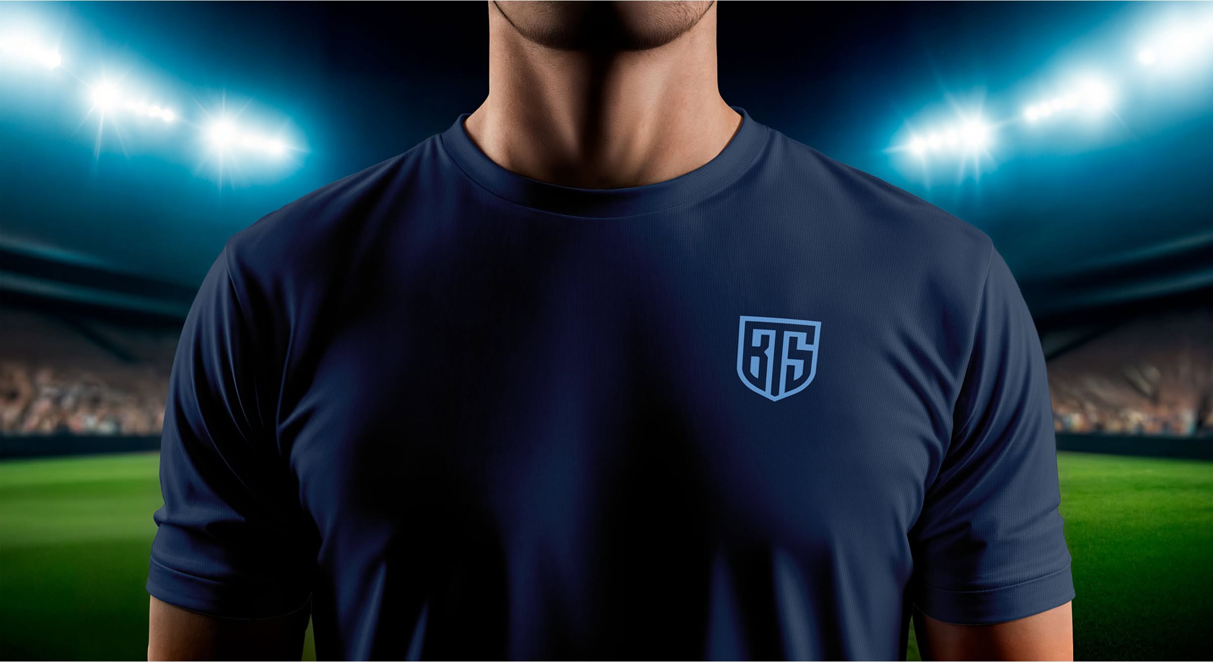 BTS-Shirt A person in a dark blue shirt with bright blue shield logo in a brightly lit stadium at night. The logo contains the letters "BTS." The atmosphere is intense and focused, with a blurry crowd in the background.