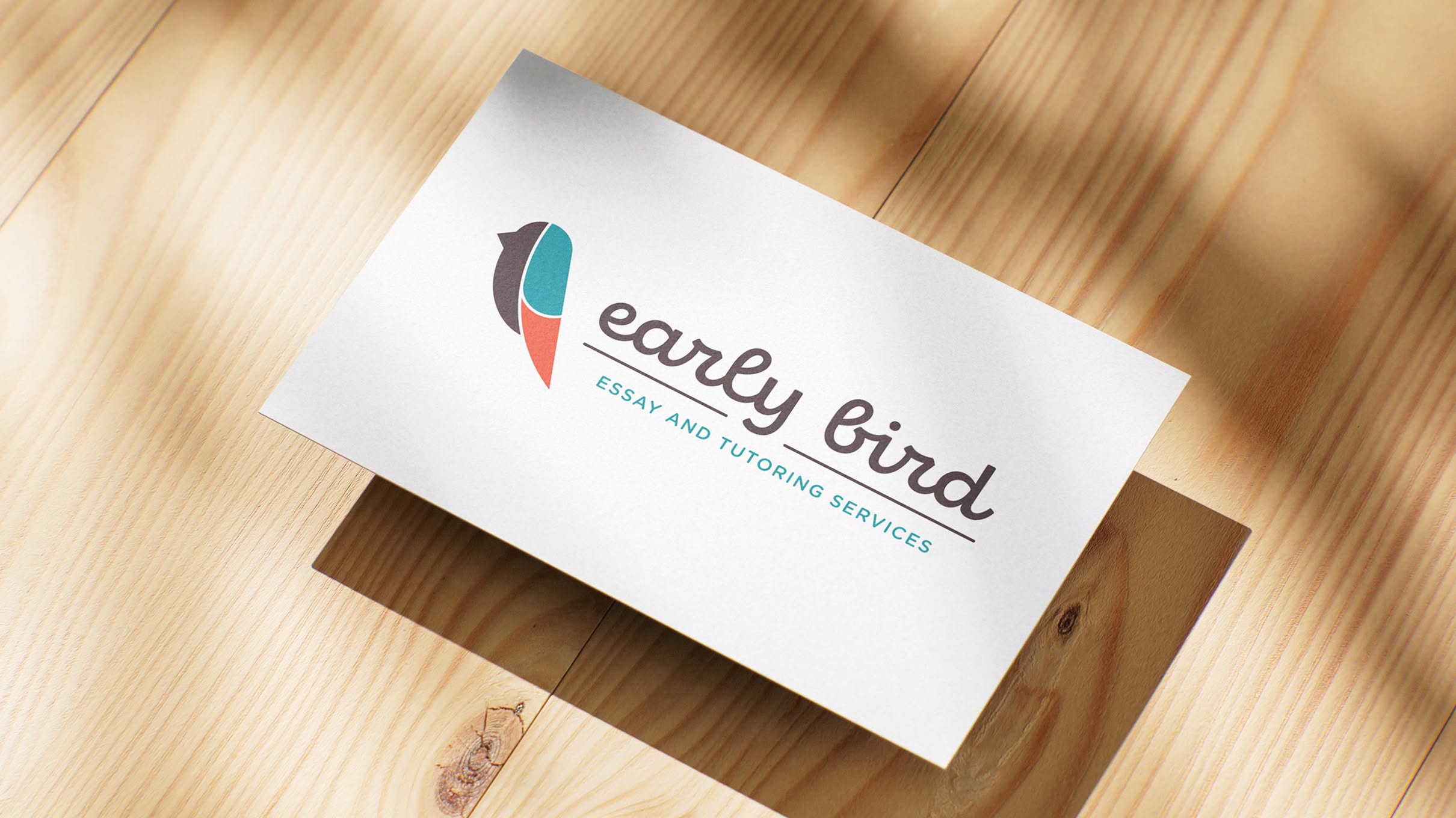 EarlyBird-Hero A business card on a wooden surface, featuring the logo for Early Bird Tutoring. The logo includes stylized bird in brown, blue, and red. Text to the right reads "early bird" in cursive, with "Essay and Tutoring Services" below.