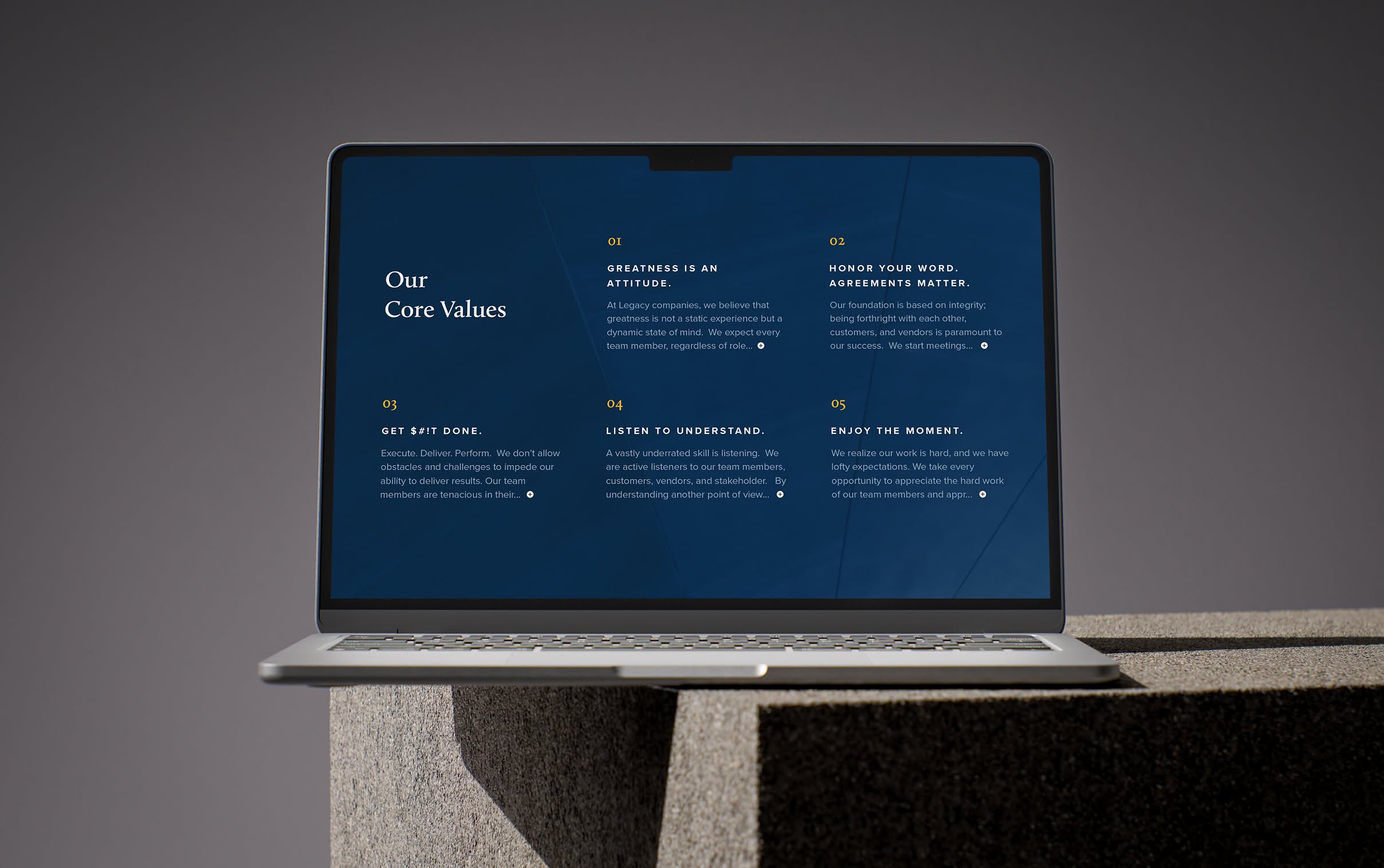 Legacy-Laptop A laptop displaying a page from the Legacy Companies website with text titled "Our Core Values" on a dark blue screen. The laptop rests on a concrete surface, conveying a professional, modern tone.