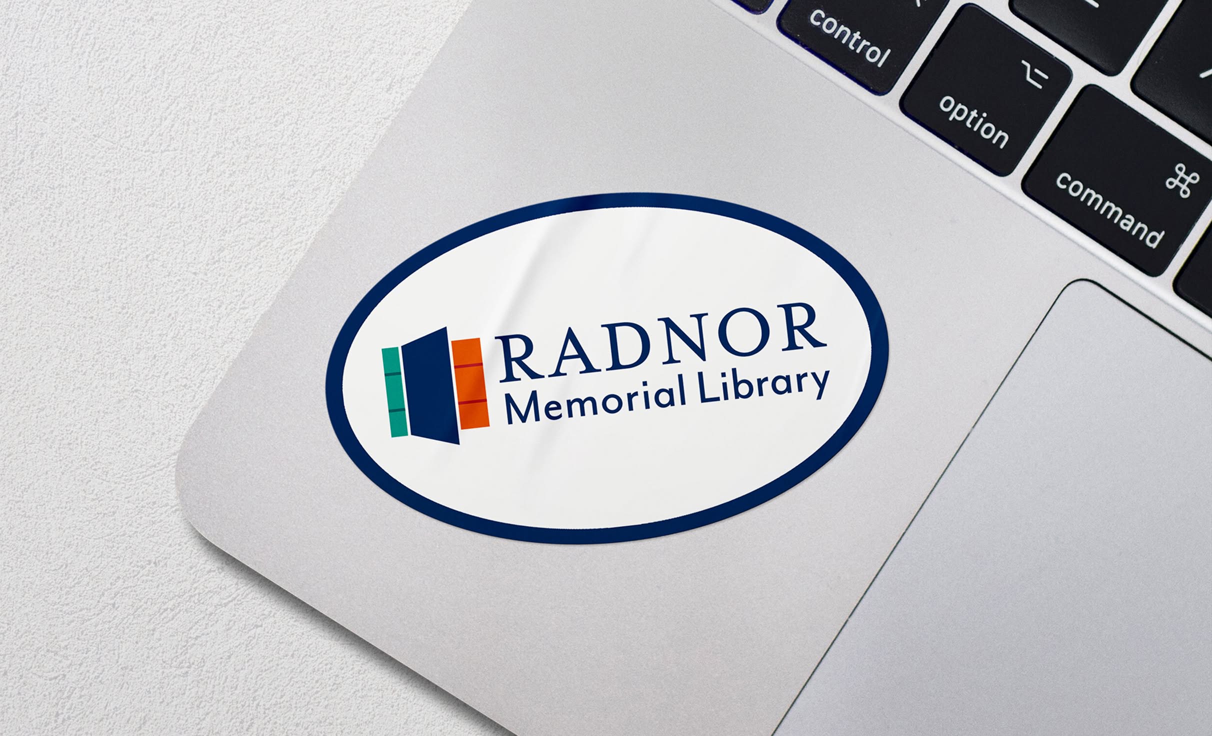 RML-Sticker Oval sticker on a laptop shows the Radnor Memorial Library logo featuring green, navy, and orange rectangles.